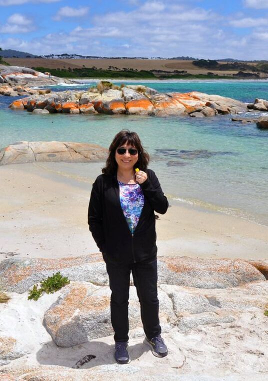 Woman smiling in front ot the sea. Brightly coloured rocks adorn the seascape