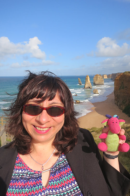 photo of Bel at the 12 apostles (rock formations in near the Great Ocean Road, Victoria, Australia). She is holding a small toy dragon, coloured bright pink and green